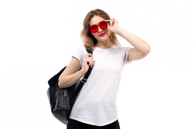Вид спереди барышня в белой футболке, красные очки, черная сумка, улыбается на белом