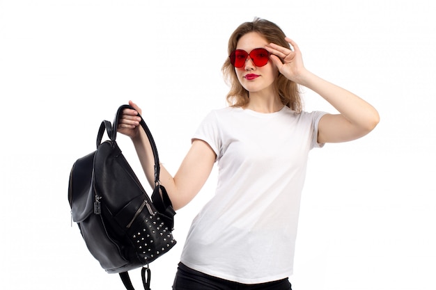 A front view young lady in white t-shirt red sunglasses holding black bag smiling on the white