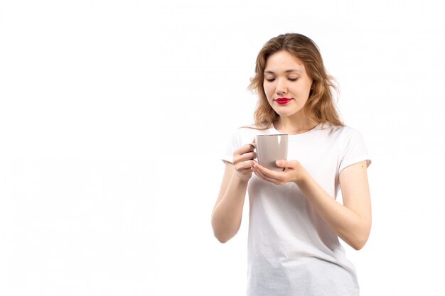 A front view young lady in white t-shirt smiling holding cup with tea on the white