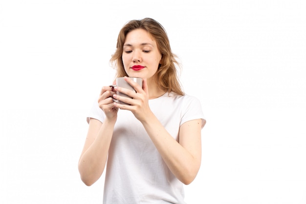 A front view young lady in white t-shirt smiling holding cup with tea on the white