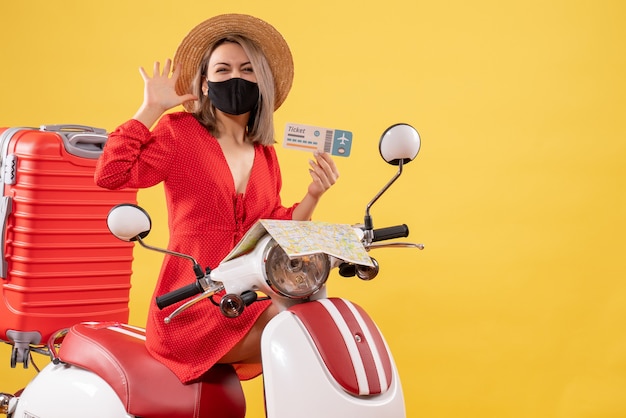 Front view of young lady with black mask on moped holding ticket waving hand