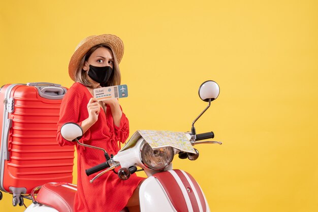 Front view young lady with black mask on moped holding up ticket