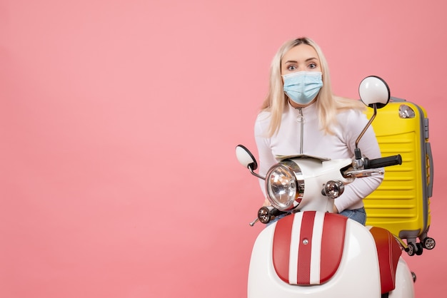 Front view young lady with mask on moped with yellow suitcase