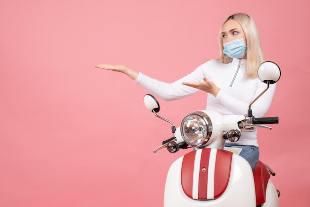 Foto gratuita giovane signora di vista frontale con la maschera che indica a sinistra che sta vicino al ciclomotore