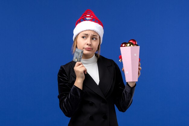 Вид спереди юная леди с елочными игрушками и банковской картой на синей стене новогодние эмоции праздники