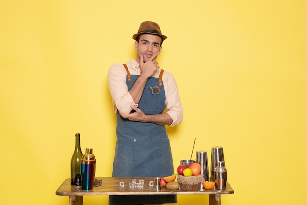 Вид спереди молодой мужчина-бармен перед столом с коктейлями на желтом фоне