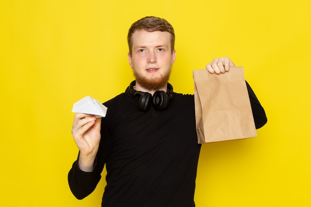 Front view of young male in black shirt holding paper plane and good package