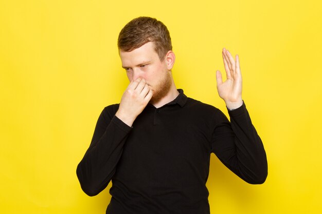 Front view of young male in black shirt posing and closing his nose due to smell