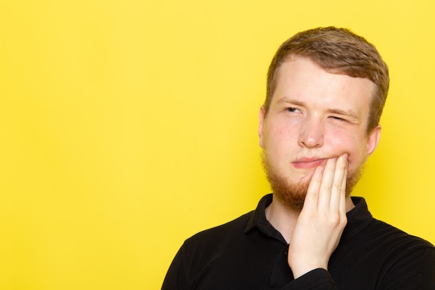 Front view of young male in black shirt posing and having a toothache