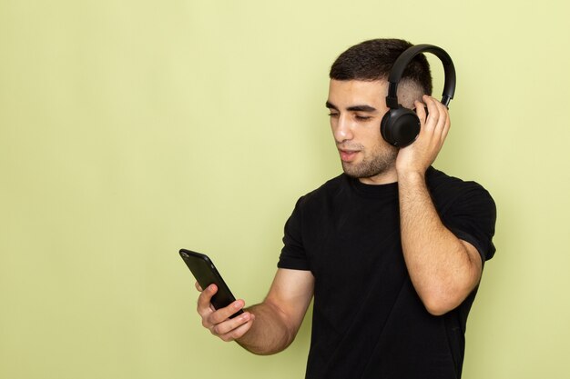 携帯電話を押しながら緑で音楽を聴く黒いtシャツで正面の若い男性