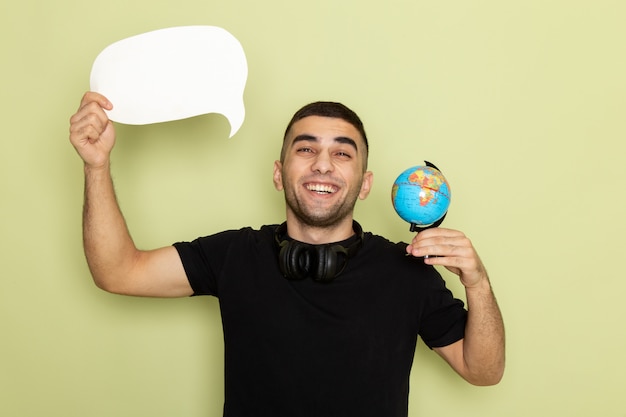 Free photo front view young male in black t-shirt holding white sign and little globe with smile on green