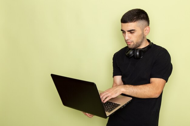 Front view young male in black t-shirt using laptop on green