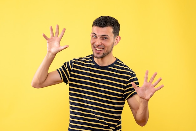 黄色の孤立した背景に手を開く黒と白の縞模様のTシャツの正面図若い男性