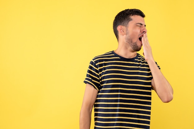 Front view young male in black and white striped t-shirt yawning on yellow isolated background