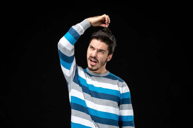 Free photo front view young male in blue striped jersey pulling his hair on a black wall