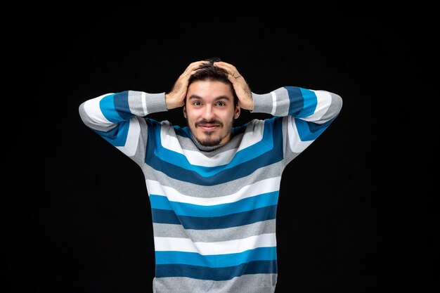 Front view young male in blue striped jersey smiling on black wall