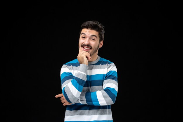 Front view young male in blue striped jersey thinking and smiling on black wall