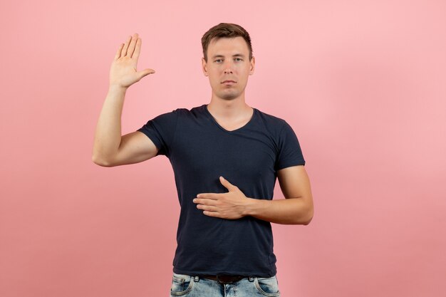 Front view young male in blue t-shirt posing with one raised hand on pink background male emotion color model human