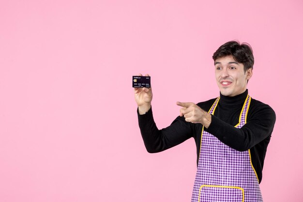 Front view young male in cape holding bank card and pointing on pink