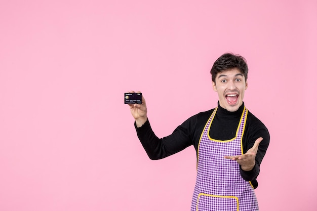 Вид спереди молодой мужчина в плаще держит банковскую карту и радуется на розовом фоне горизонтальный рабочий цвет униформы работа кулинария шеф-повар кухни