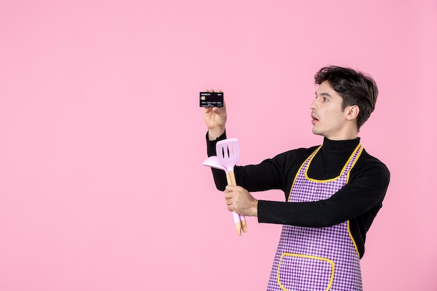 Front view young male in cape holding bank card and spoons on pink background uniform job worker color money horizontal cuisine profession chief