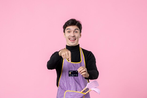 Front view young male in cape holding black bank card on pink background job profession cooking chief cuisine worker color money horizontal