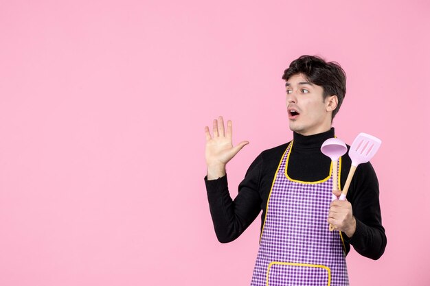 Front view young male in cape holding pink spoons on pink