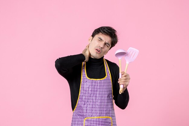 Front view young male in cape holding spoons on pink background profession food horizontal uniform dough cuisine work colors cooking meal