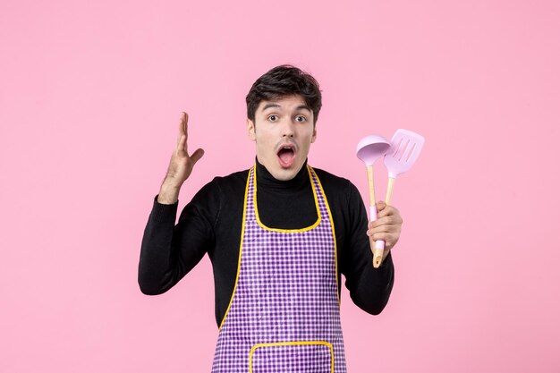 Front view young male in cape holding spoons on pink background profession food horizontal uniform dough work color cooking meal