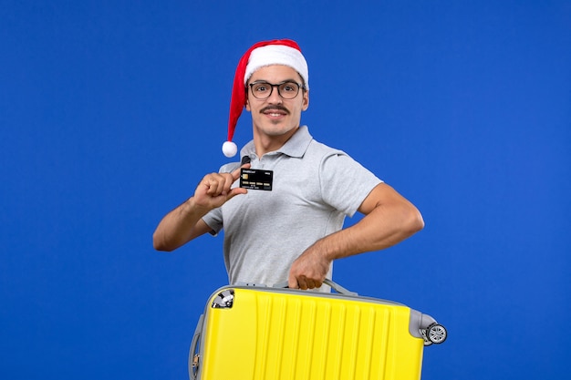 Front view young male carrying bag and bank card on blue wall flight vacation plane