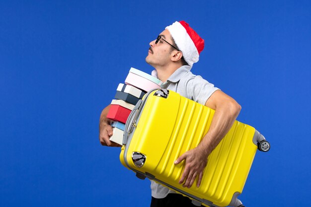 Front view young male carrying bag and presents on blue wall flights vacation planes