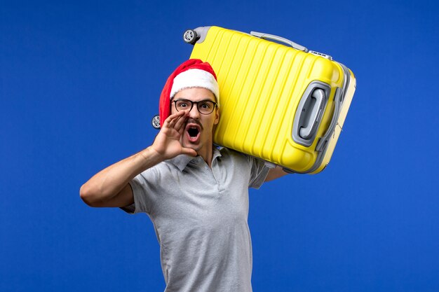 Front view young male carrying heavy bag on blue wall flight plane vacation