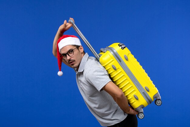 Front view young male carrying heavy bag on blue wall flights vacation plane