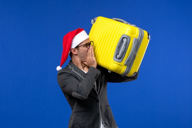 Front view young male carrying heavy yellow bag on blue desk flight plane vacation