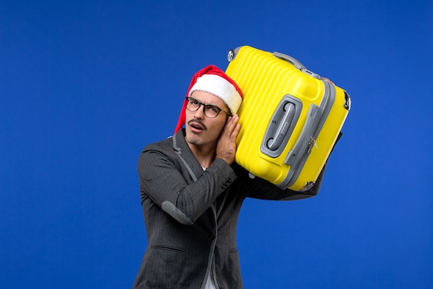 Front view young male carrying heavy yellow bag on the blue wall flight plane vacation