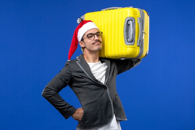 Front view young male carrying heavy yellow bag on blue wall flights planes vacation