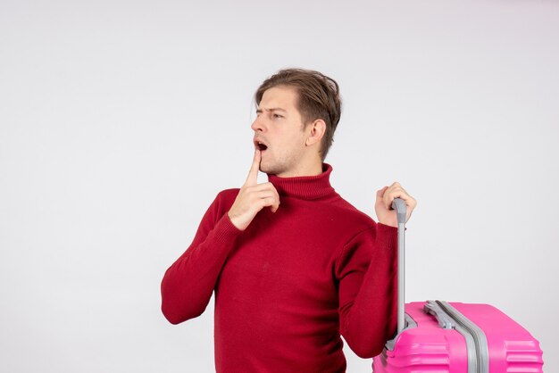 Вид спереди молодого мужчины, несущего розовую сумку на белой стене