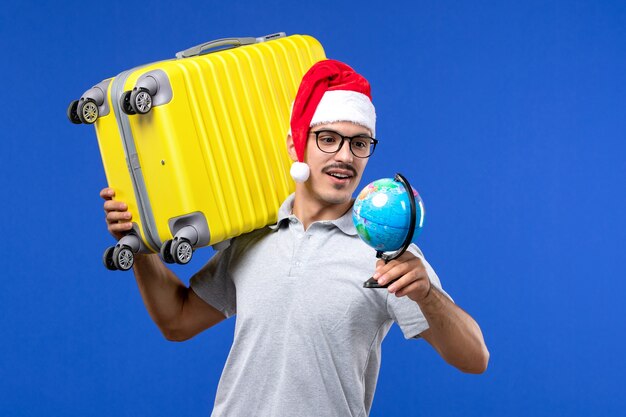 Giovane maschio di vista frontale che trasporta borsa gialla sul maschio blu di viaggio di vacanza dell'aereo della parete