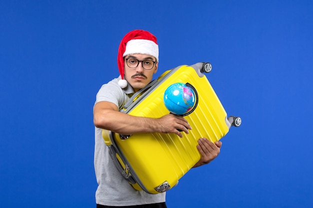 青い壁の旅の感情の休暇で地球と黄色のバッグを運ぶ正面図若い男性