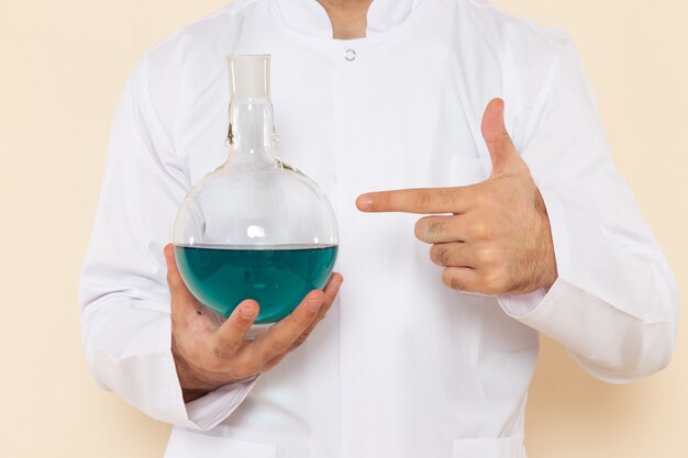 크림 벽 과학 실험 화학 과학에 파란색 솔루션 플라스크를 들고 흰색 특수 정장에 전면보기 젊은 남성 화학자