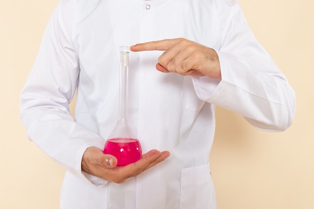 クリーム色の壁の科学実験化学科学のピンクのソリューションとフラスコを保持している白い特別なスーツの正面図若い男性の化学者