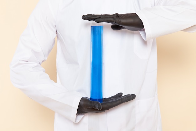 Front view young male chemist in white special suit holding a little flask with blue solution on cream wall lab chemistry science experiment