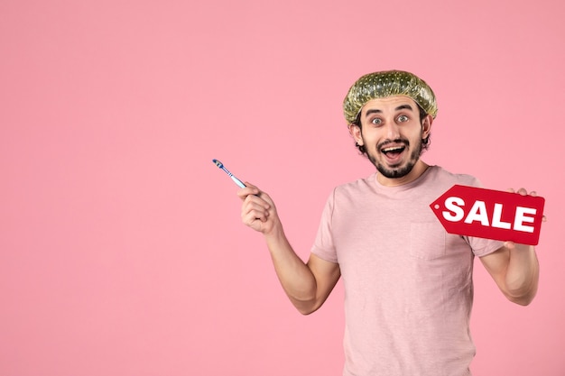 front view young male cleaning his teeth and holding sale nameplate on pink background