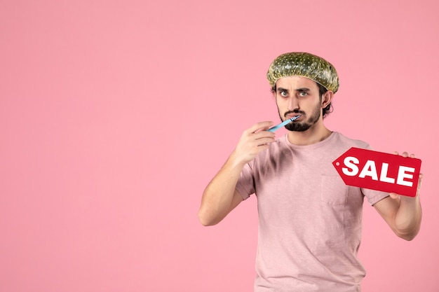 вид спереди молодой мужчина чистит зубы и продает табличку на розовом фоне