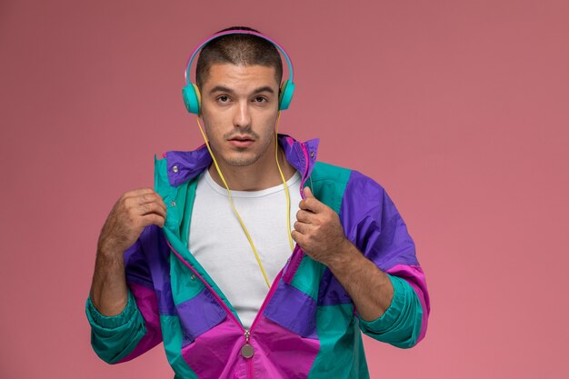 Front view young male in colorful coat posing and listening to music on pink background