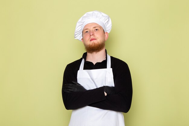 검은 장갑 포즈에 흰색 케이프 흰색 머리 모자와 검은 셔츠에 전면보기 젊은 남성 요리사
