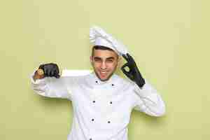 Бесплатное фото Вид спереди молодого повара в белом костюме повара в темных перчатках и с острым ножом на зеленом
