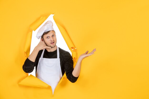 正面図若い男性料理人白いマントと黄色の破れた背景の帽子で料理の仕事白人男性料理写真カラーキッチン