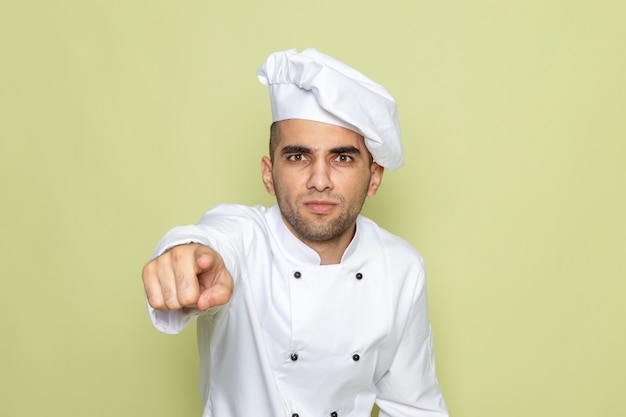 Front view young male cook in white cook suit pointing out with anger on green