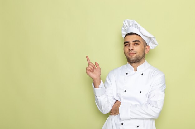 Front view young male cook in white cook suit standing with thinking expression on green